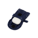 A sleek, white oval earbuds case is nestled inside the Baggu Puffy Earbuds Case, featuring a dazzling constellation pattern on navy with velcro closures.