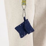 The Baggu Earbuds Case - Constellation Navy, a blue fabric pouch with a constellation pattern, hangs from a clip on a strap against a neutral background.