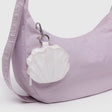 A light purple Baggu shoulder bag with a fabric strap features a Shell Charm - Pearl Metallic coin purse as a fun accessory, attached by a silver clip.