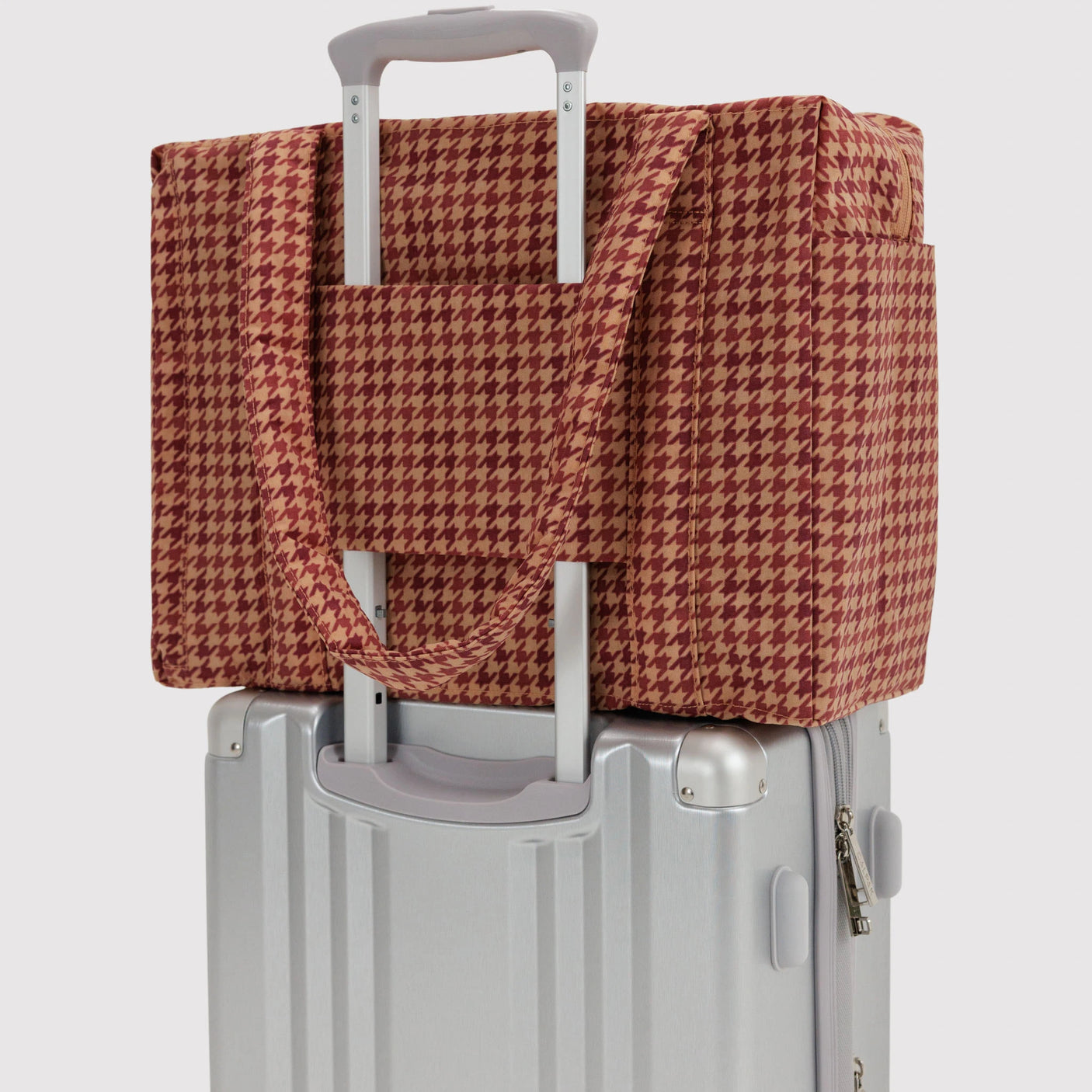 Houndstooth carry-on bag over suitcase handle, tan and dark red pattern