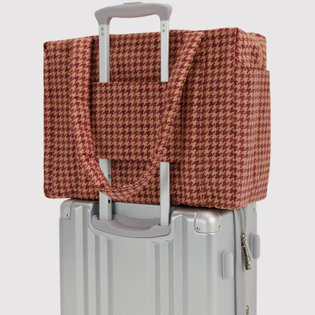 Houndstooth carry-on bag over suitcase handle, tan and dark red pattern