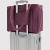Plum carry-on tote bag with strap, slid over a luggage handle on a suitcase