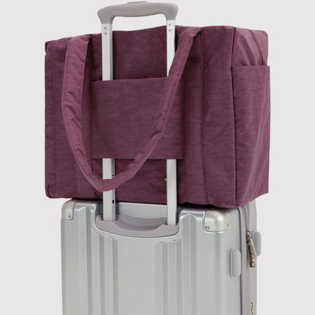 Plum carry-on tote bag with strap, slid over a luggage handle on a suitcase