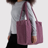 Plum zip-top tote bag with two handles and front pockets, carried over shoulder