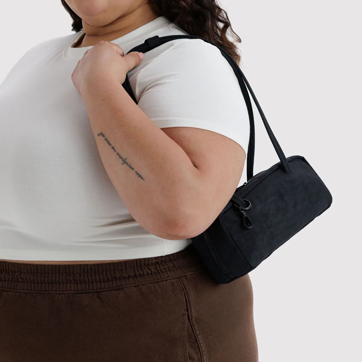 Small bowler bag in black worn crossbody with adjustable strap and zip top.