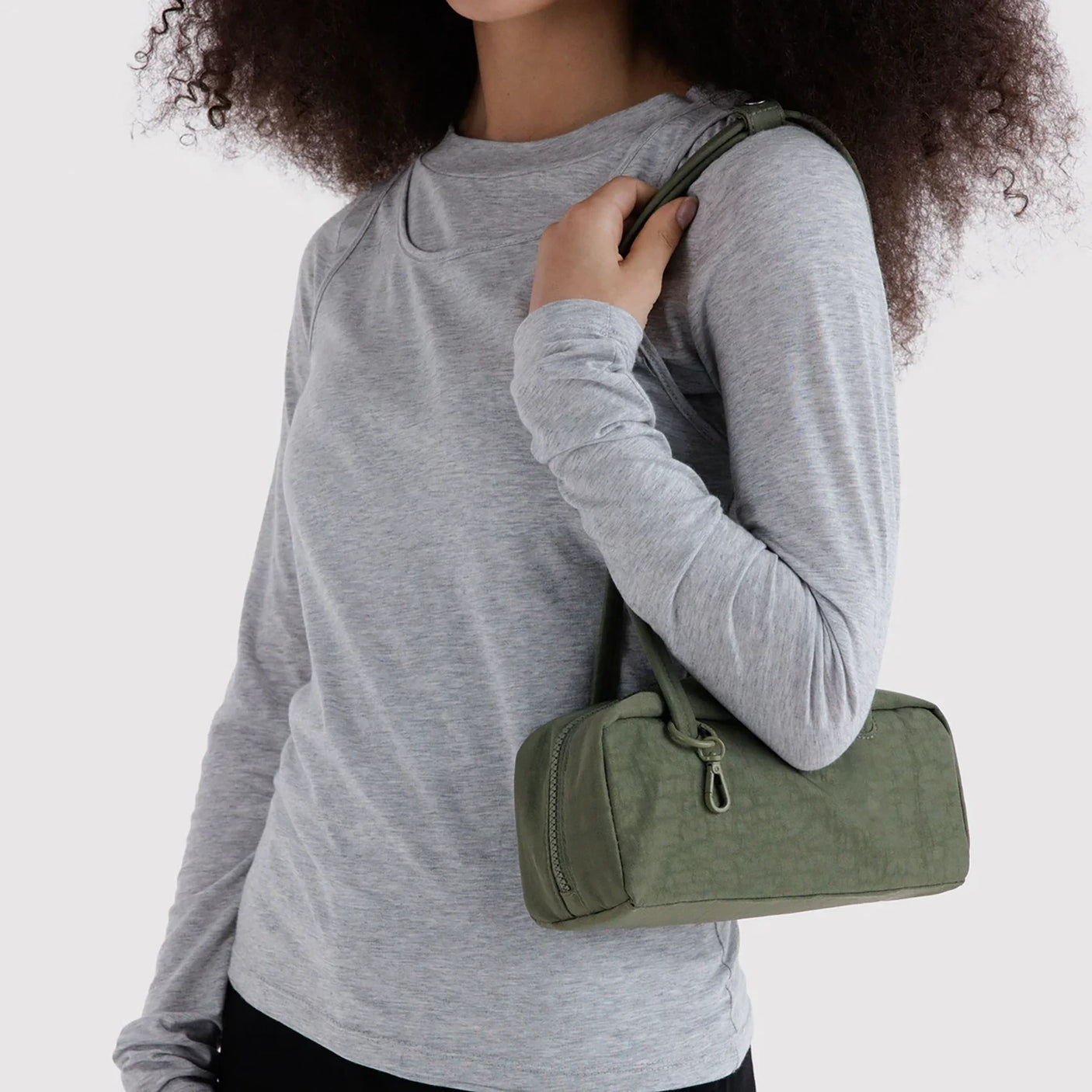 Olive small bowler bag on shoulder with two top handles and zipper closure.