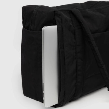 A sleek silver laptop peeks out from the side pocket of the Baggu Small Cloud Carry-on - Black, crafted from recycled heavyweight nylon, its modern design perfectly complementing the black bag's elegant fabric.