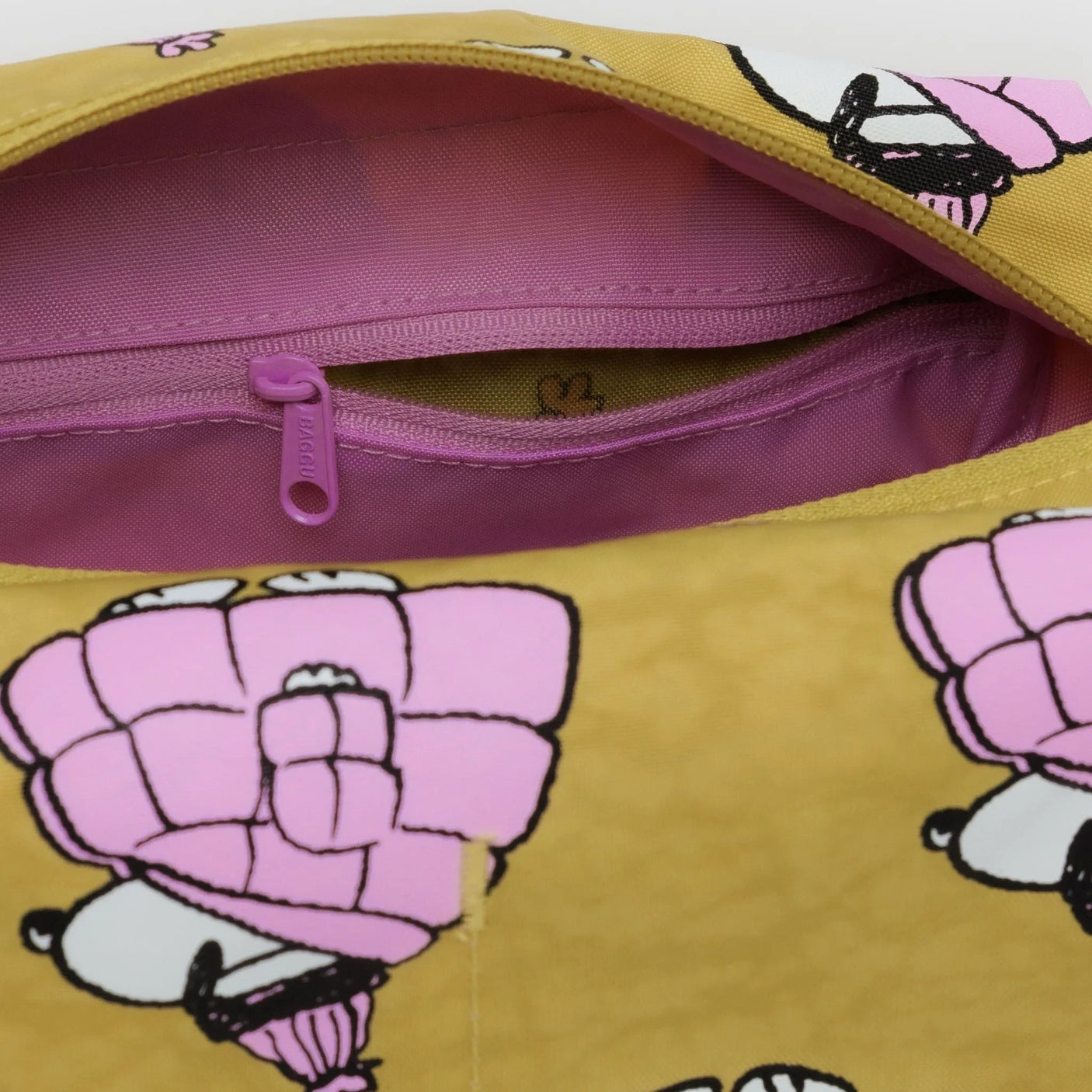 Close-up of the yellow Peanuts x Baggu - Toiletry Dopp Kit - Puffer Snoopy by Baggu, showcasing a purple zipper and a cartoon pattern of Snoopy holding a pink umbrella-like object.