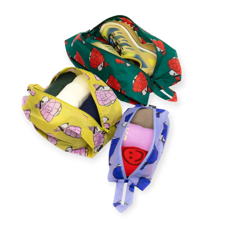 The Peanuts x Baggu Storage & Travel Set by Baggu includes three zippered pouches made from recycled nylon. Each pouch features a unique turtle design in green, yellow, and purple, perfect for organizing your essentials during travel.