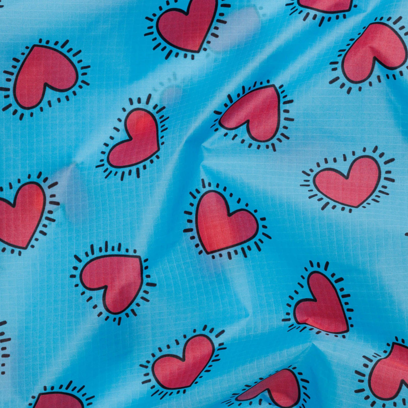 The Baggu Standard Bag - Keith Haring Hearts by Baggu features a vibrant design on blue fabric, adorned with multicolored hearts outlined by black dashes, inspired by Keith Haring's iconic style. Crafted from recycled nylon, this bag is both eco-friendly and artistically dynamic.