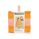 Folded Baggu Standard Reusable Bag - Tangerine Stripe in packaging, featuring a label with an image of a person holding the recycled nylon bag, in orange and pink tangerine stripes.