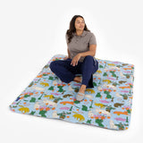 An individual relaxes on the Baggu Puffy Picnic Blanket - Table Cats, showcasing whimsical cat illustrations on a simple light backdrop.