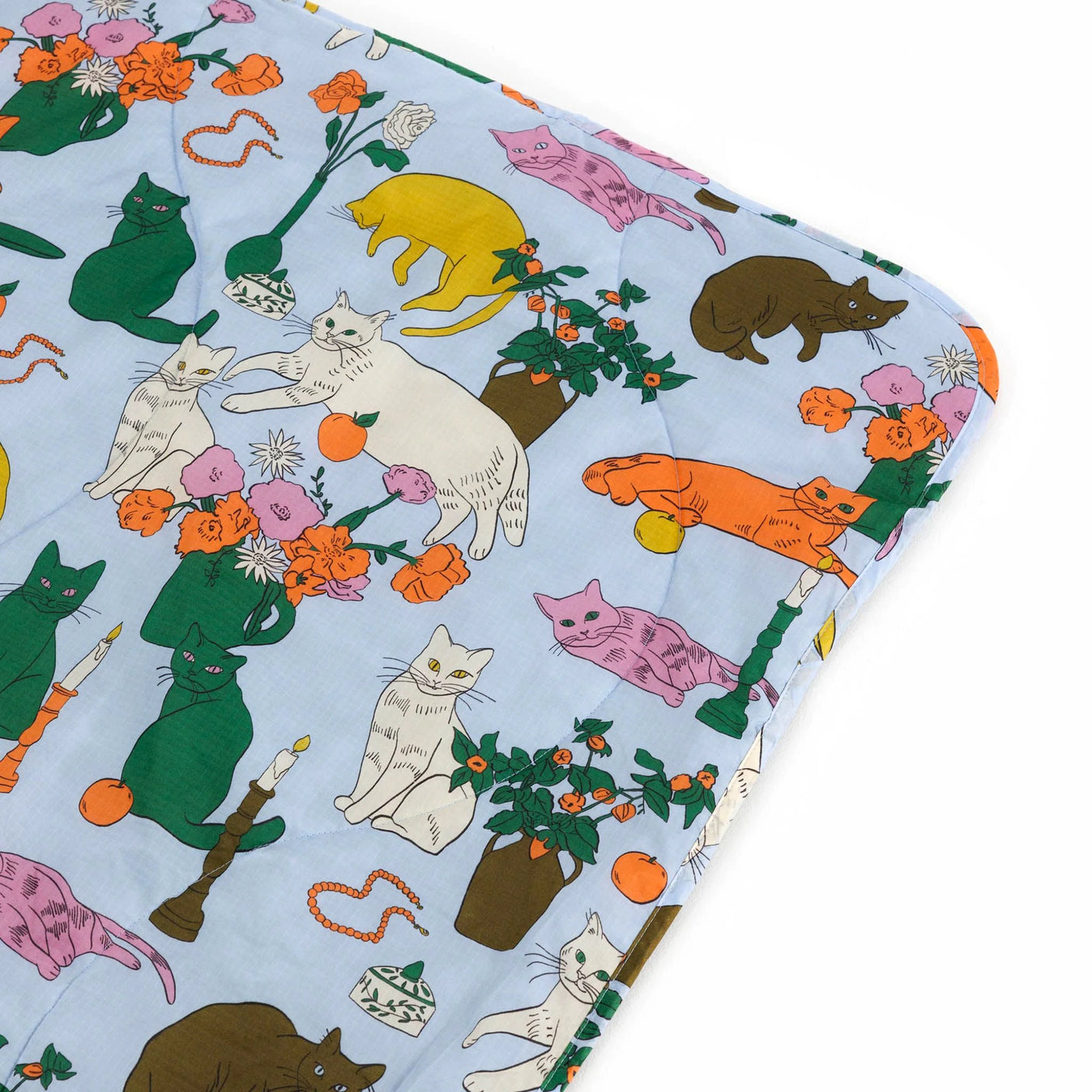 The Baggu Puffy Picnic Blanket - Table Cats features a vibrant, eco-friendly design with cartoon cats playfully posed among flowers, vases, and candles—ideal for a cheerful picnic outing.