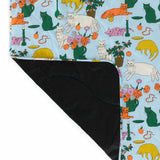 The Baggu Puffy Picnic Blanket - Table Cats, designed by Baggu, showcases a colorful array of playful cat illustrations and vibrant flowers on one side, complemented by a plain black fabric on the other, embodying sustainable design in every thread.