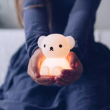 A person clad in a dark long-sleeved garment holds the Boris Bear Miffy Night Light (15cm) from the Miffy brand in both hands. This charming bear-shaped lamp, crafted from BPA-free silicone, emits a gentle glow ideal for creating cozy atmospheres.