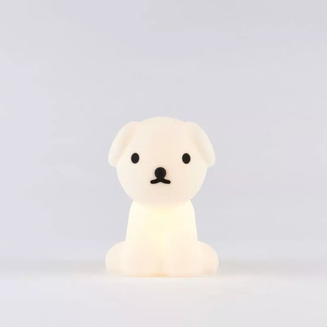 The Snuffy Dog Miffy Night Light (15cm) by Miffy, made from BPA-free silicone, softly glows against a simple gray backdrop. Its delightful design, inspired by Miffy and Friends, showcases black accents that animate this small white dog-shaped lamp.