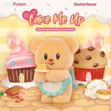 Soft plush bear in blue apron holding tiny cake with cupcake and cookie house background in pastel tones