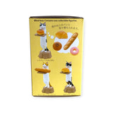 The Kitan Club Cat Bakery Waiter Blind Box features a collectible cat figurine as a bakery waiter, holding pastries against a yellow background. Japanese text and images of various bakery treats enhance this whimsical display.