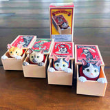 Four Kitan Club Cat in a Matchbox Blind Box figurines are cozily set in vivid matchbox-style boxes, each paired with a colorful design card and elegantly arranged on a wooden surface.