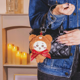 Brown teddy bear plush keychain with red ribbon hanging from a handbag strap and clip.