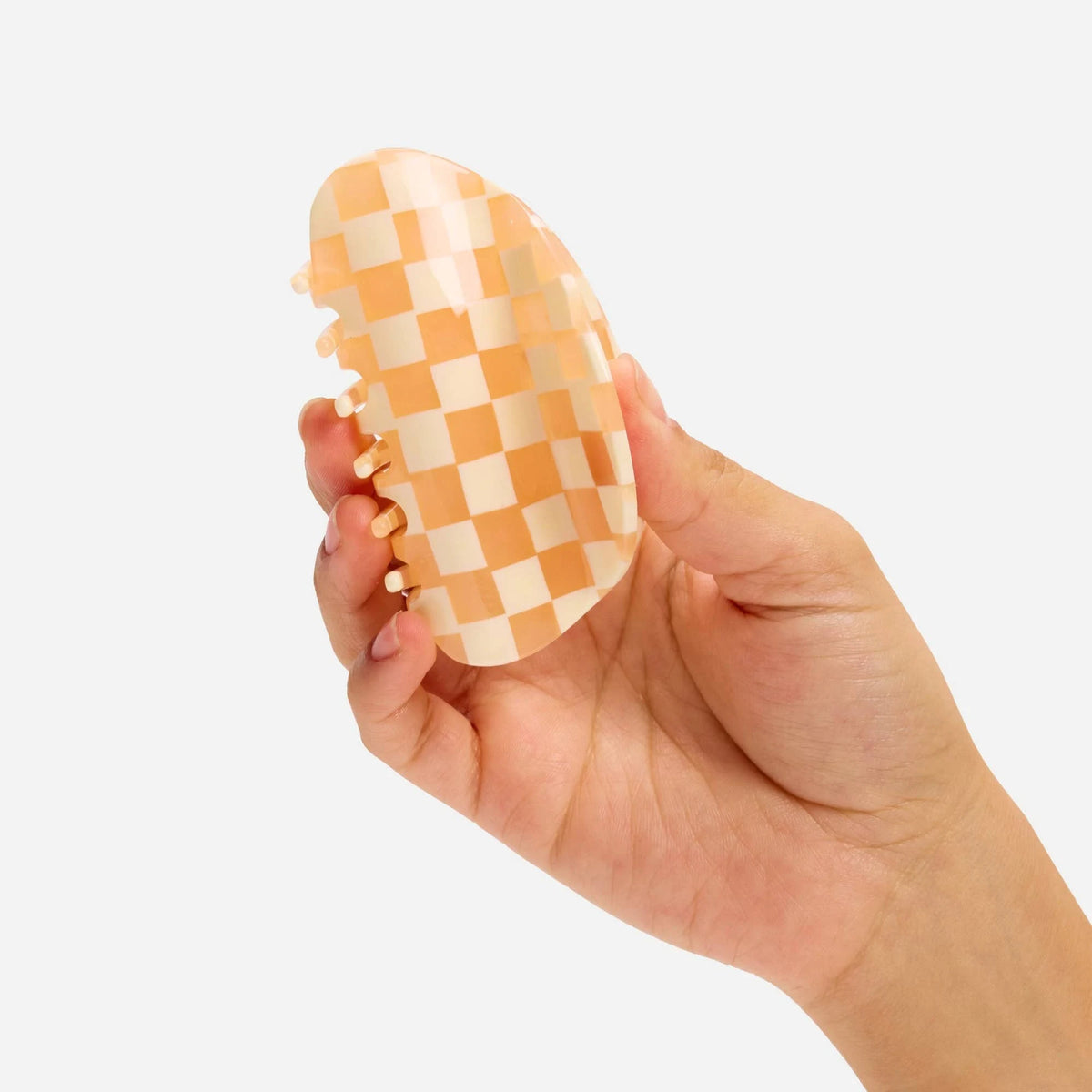 Peach checkered hair claw clip held from side, visible teeth