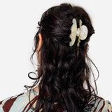 Octopus claw hair clip in translucent pearl-shimmer cream on dark wavy hair.
