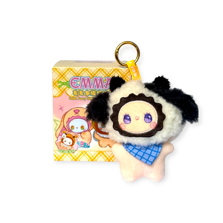 The Lucky Emma Emma Fuzzy Family Bag Charm - Blind Box features a plush keychain with black ears, a blue scarf, and purple eyes beside its colorful blind box package decorated with playful cartoon designs.