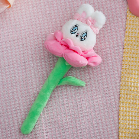 White Esther Bunny plush with pink flower petals and green stem lying on textured pink and yellow fabric background