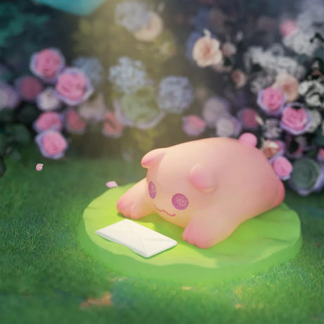 Soft pink ShinWoo Secret Bear figure with glitter eyes lying on green base near white envelope in blurred garden setting