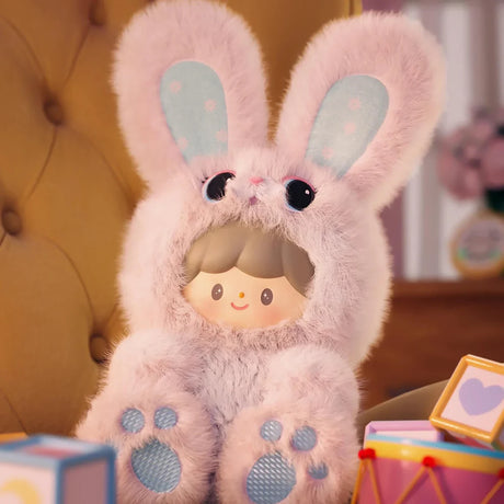 Plush keychain featuring a character dressed in a soft pink bunny outfit with floppy ears and blue paw pads seated indoors