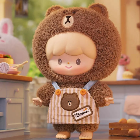 Plush figure dressed in a fuzzy brown bear costume with striped apron and blonde hair in a cozy indoor setting