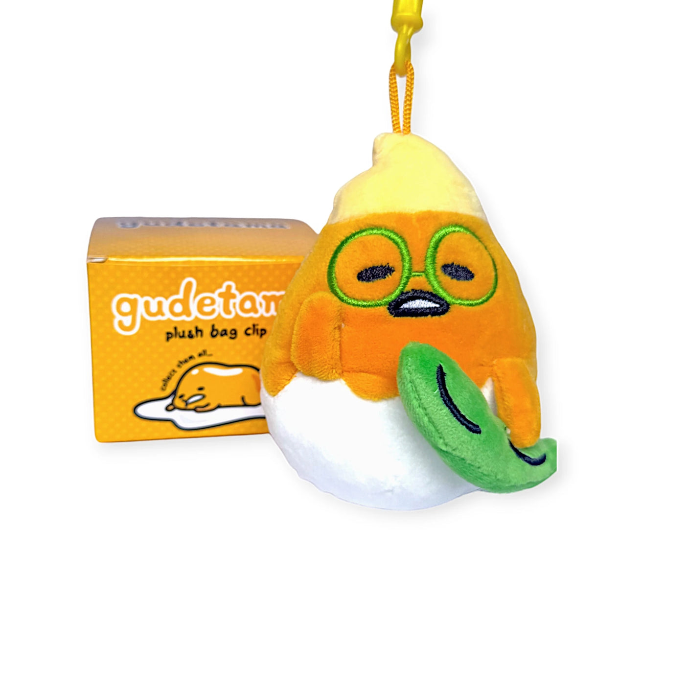 A plush Gudetama keychain dressed as a peeled egg with glasses and a green leaf is featured in the "Gudetama Bag Clip - Blind Box." The box displays an image of Gudetama, ideal for adding charm to your keys or bag.