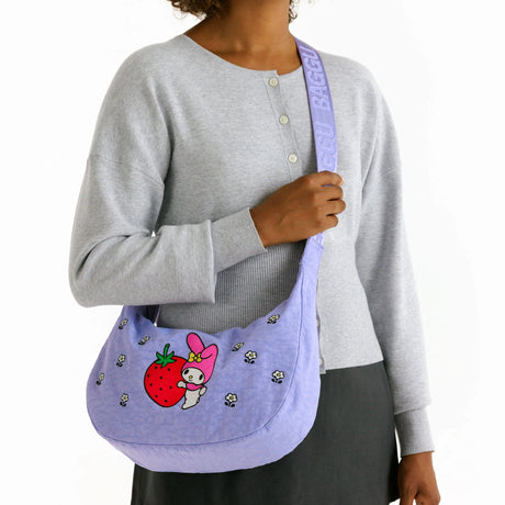 Model holding lavender Hello Kitty x Baggu Medium Nylon Crescent bag with My Melody and strawberry graphic, promo image 1