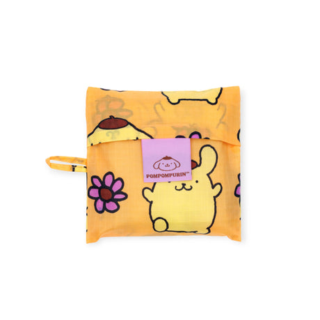 The Baggu Standard Baggu x Hello Kitty - Pompompurin features a yellow design with flowers and cartoon characters, folds into a pouch with a purple Pompompurin logo flap, and is made from limited edition recycled nylon.