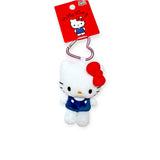 The Hello Kitty - Heart Clasp Keychain showcases a Hello Kitty plush in a blue outfit with a red bow. It includes a metal clip and red tag, making it an ideal collectible for fans.