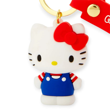 The Hello Kitty 3D Figure Keychain showcases the beloved character in a blue dress, red bow, and red-and-white striped shirt, attached to a vibrant red strap with a metal button, encapsulating the timeless charm of Hello Kitty you love.