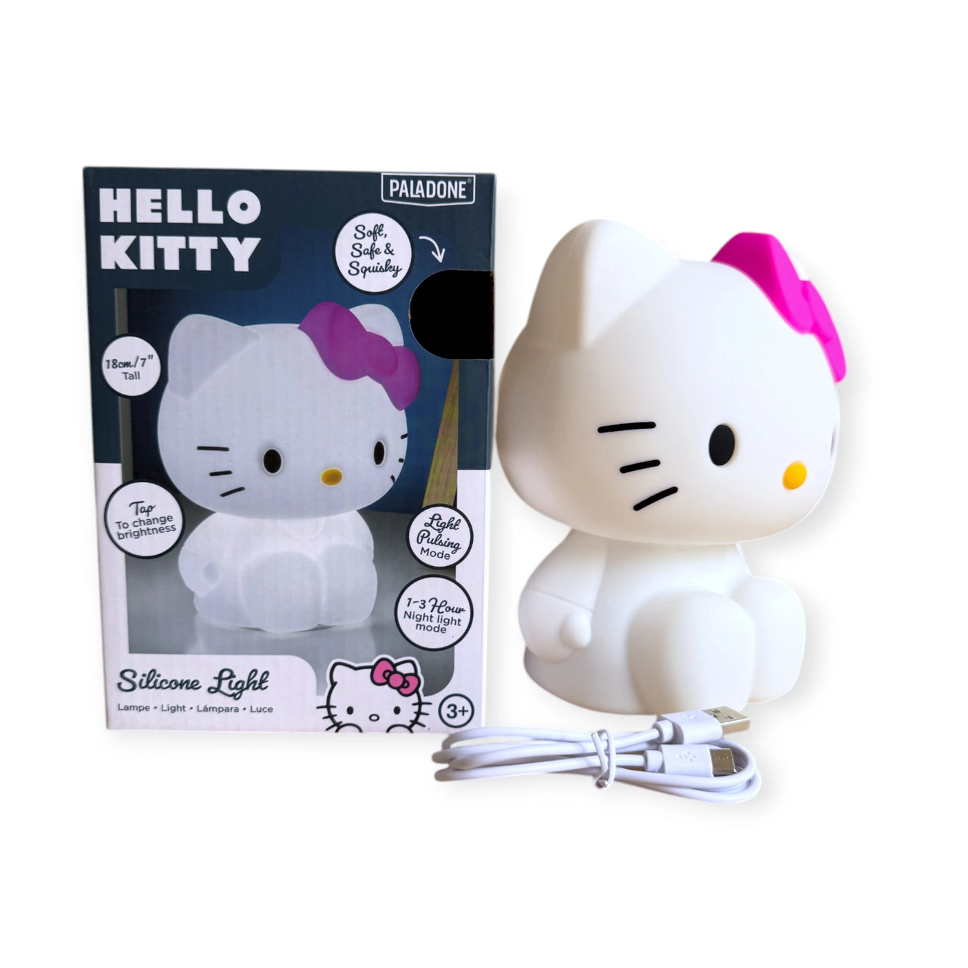 The Hello Kitty Silicone Night Light, with a pink bow and displayed in front of its packaging, includes a charging cable. This squishy light creates a cozy glow and is ideal for ages 3 and up.