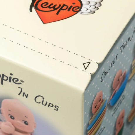 Close-up of cream-colored product box corner with red heart and partial illustrations of small doll figures on light blue background