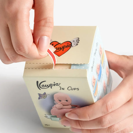 Person peeling open cream-colored box with Kewpie logo and baby doll illustration on white background