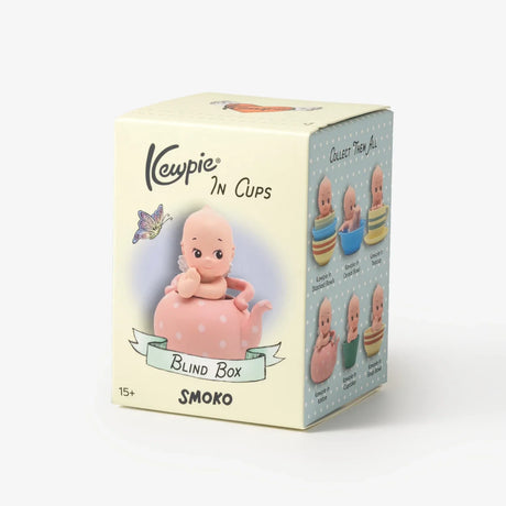 Small doll figure sitting inside pink polka-dot teapot on a pale yellow blind box with illustrations and text
