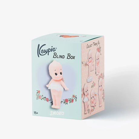 Cream-colored blind box packaging featuring illustration of small baby doll figure with a pink scarf and floral accents