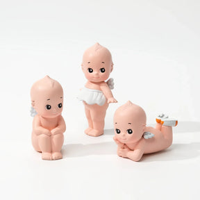Three small bald baby doll figurines with tiny wings posed against a white background