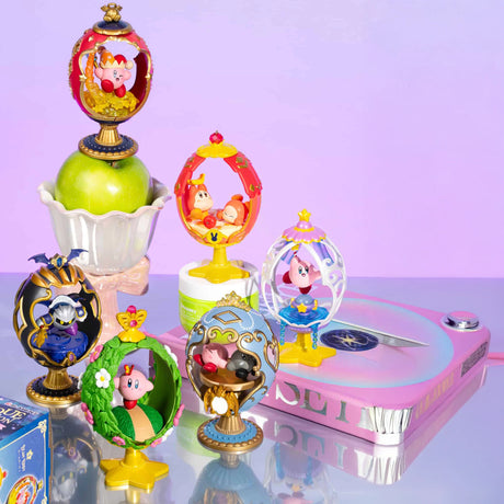 Kirby Ovaltique Globe Blind Boxes by Re-Ment, filled with colorful figures in egg-shaped containers, are arranged on a reflective surface beside an apple in a glass bowl and a pink rotating platform featuring a compass design.