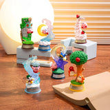 Six Kirby figures from the Re-Ment Kirby Blind Box - Dream Land series are displayed on a wooden surface, showcasing Kirby in playful scenes. Nearby, a glowing lamp and book add a cozy touch, making it feel like unboxing Re-Ment's endless charm and creativity!.