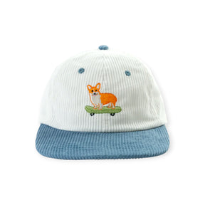 White corduroy hat with blue brim and embroidered corgi standing on green skateboard on front panel