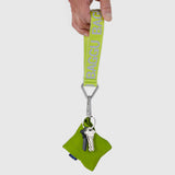 A hand holds a Baggu Logo Keychain - Citron with a green strap and two keys, accompanied by a small pouch made from recycled nylon.