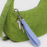 A chic green bag with a matching strap features two keys on a Baggu Logo Keychain - French Blue, clipped by a carabiner. The vibrant strap is labeled "Baggu," blending style with functionality.