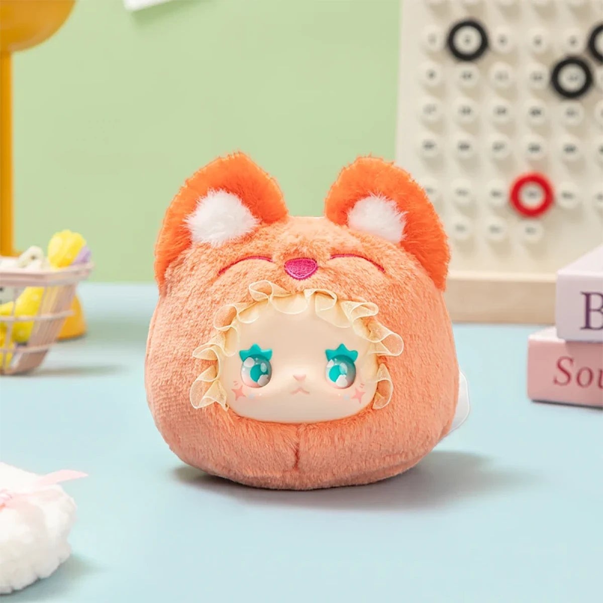Plush Lovely Emma Rua Rua Zoo bag charm in orange fox costume with ruffled hood and large blue eyes on pastel background