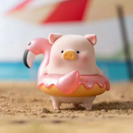 LuLu the Piggy figurine wearing a pink flamingo floatie shaped like a donut on sandy beach background