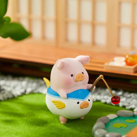 LuLu the Piggy figurine dressed as a fish costume holding a fishing rod next to a small pond on green grass